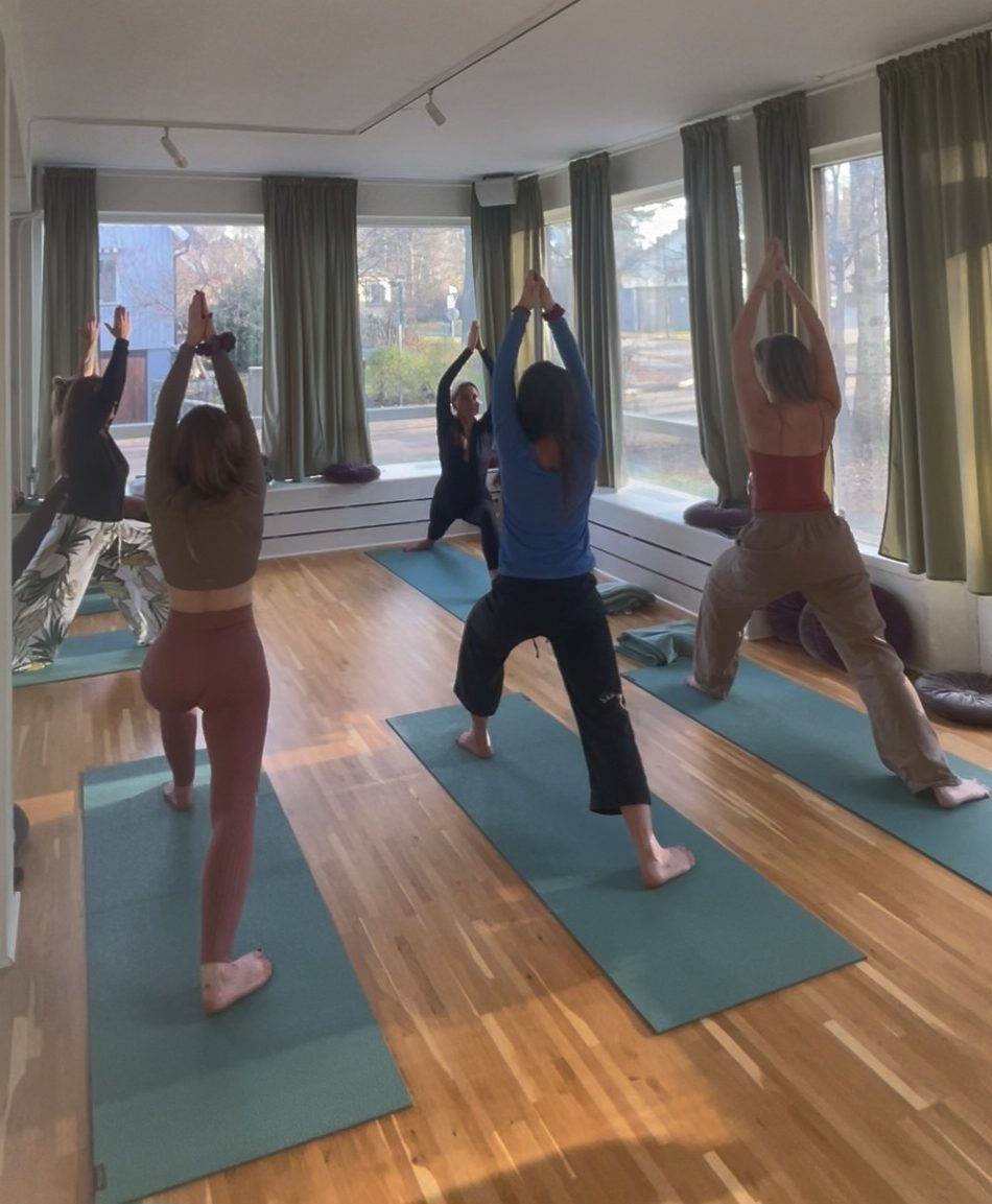 Women practising a standing yoga pose together on mats in a bright studio