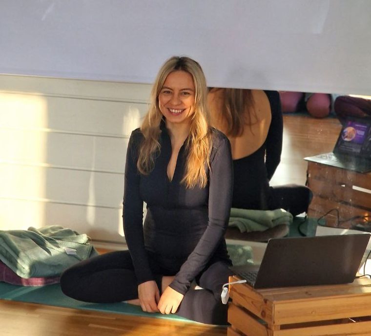 Olly sitting on a yoga mat in a sunlit studio, smiling